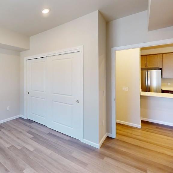 a versatile unfurnished room here at autumn haus featuring soft neutral walls, wood-style flooring, a wide sliding door closet, and recessed ceiling lighting, with an open doorway leading toward the kitchen area, creating a flexible space ideal for a bedroom, home office, or guest room.