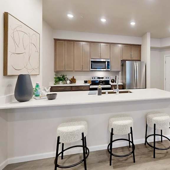 a spacious modern kitchen here at autumn haus featuring a large white island with seating for three, smooth countertops, light wood cabinetry, a built-in microwave, full-size refrigerator, and recessed ceiling lighting, complemented by wood-style flooring and an open layout that flows easily into the surrounding living area.