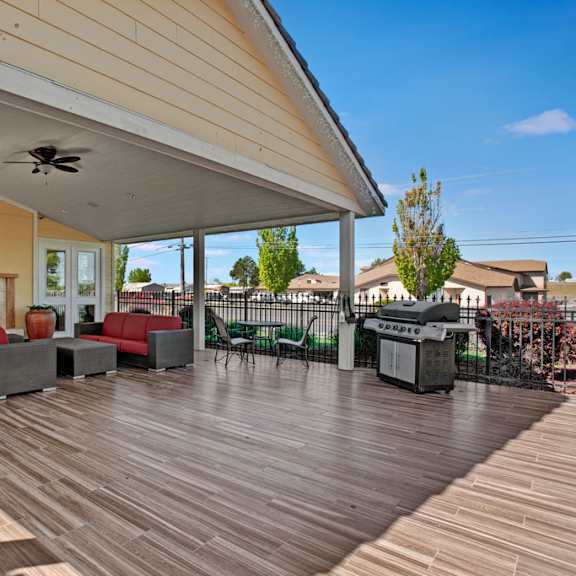 a covered outdoor patio here at the vintage with wood-style flooring, comfortable seating with red cushions, and a cozy fireplace. a built-in grill and ceiling fan create a welcoming space for relaxing and outdoor gatherings.