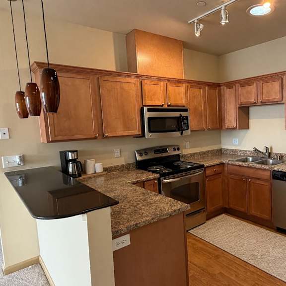 a warm kitchen here at the vintage with rich wood cabinets, speckled countertops, and stainless steel appliances including a refrigerator, stove, microwave, and dishwasher. a raised breakfast bar with pendant lighting creates a cozy and inviting dining space.