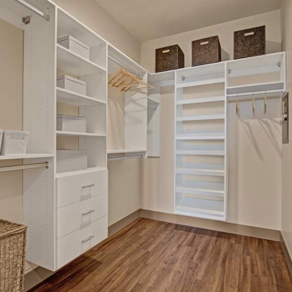 a walk-in closet with white shelving and drawers.