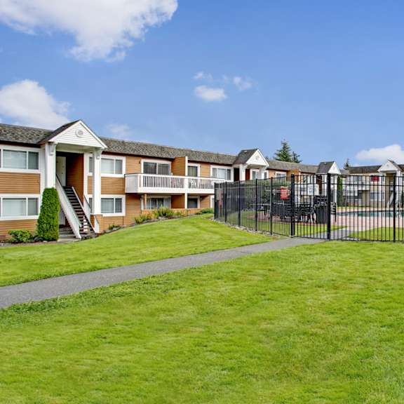 a well-maintained exterior here at whispering cedars with open green lawns, apartment buildings with private balconies, and a fenced outdoor pool area, creating a welcoming and community-focused environment.