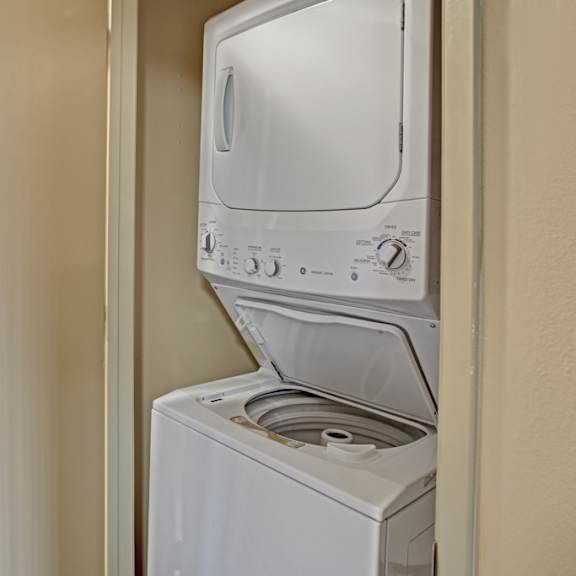 a convenient in-home laundry area here at whispering cedars with a stacked white washer and dryer tucked into a hallway closet, offering a practical and space-saving feature for easy everyday living.