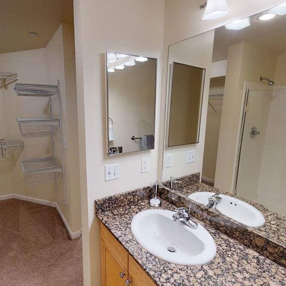 spacious admirals cove apartment bathroom with granite countertop and sink, large mirror, and walk-in closet. shower with glass door. modern, clean, and well-lit.