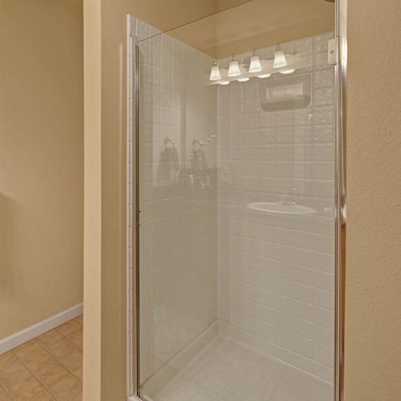 modern bathroom with beige tiles and walls, featuring a glass shower with white tiling. beige and brown towels hang on a towel rack, creating a cozy feel. located at admirals cove apartments.