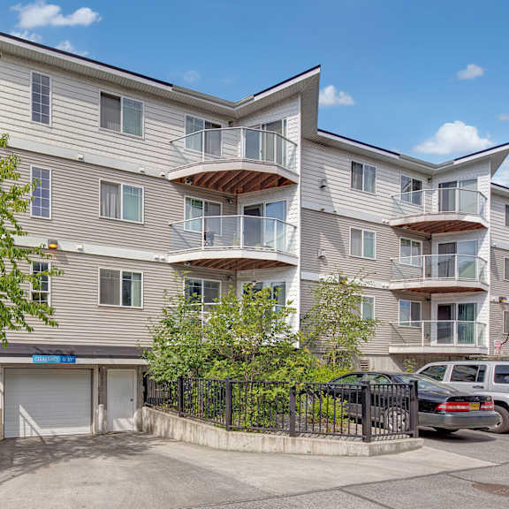 admirals cove four-story apartment building with white siding and glass balconies under a clear sky. green trees and parked cars are in the foreground.