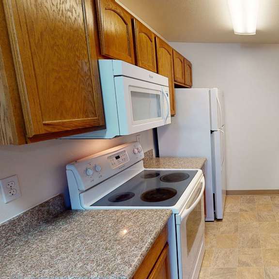 narrow kitchen with brown cabinets, granite countertops, white stove, microwave, and fridge, and a double sink with a neutral tone. amber ridge apartments.
