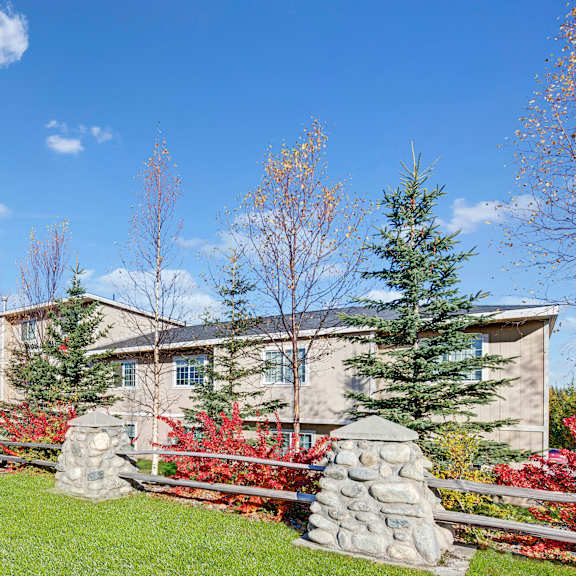 stone pillars and wooden fence enclose a building surrounded by vibrant fall trees under a bright blue sky, conveying a serene, autumnal atmosphere. amber ridge apartments.
