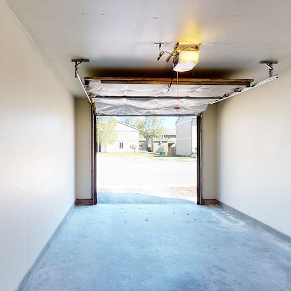 empty garage interior here at birchwood homes apartments with an open door showing a clear view of a sunny day outside. the space is clean, lit by a single ceiling light.