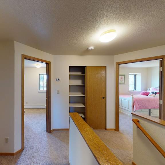 upstairs hallway here at birchwood homes apartments with beige carpet and white walls, leading to three rooms. wooden railings and doors add warmth. bright, simple, and cozy ambiance.