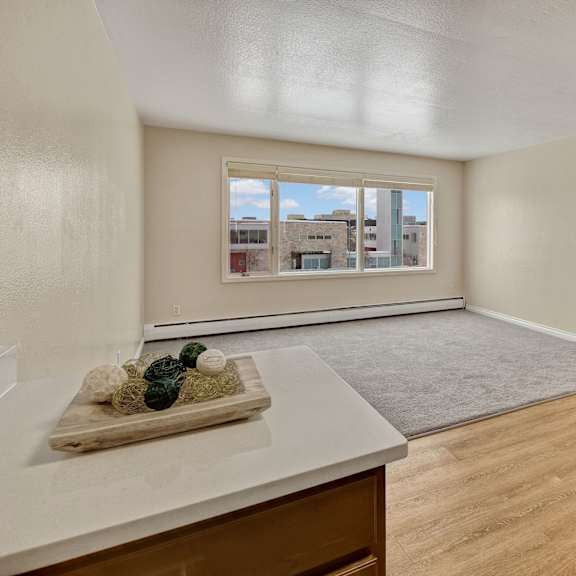 bright, modern apartment here at century plaza with beige walls and light wood flooring. a large window offers urban views. decorative balls sit on a counter next to a fridge.