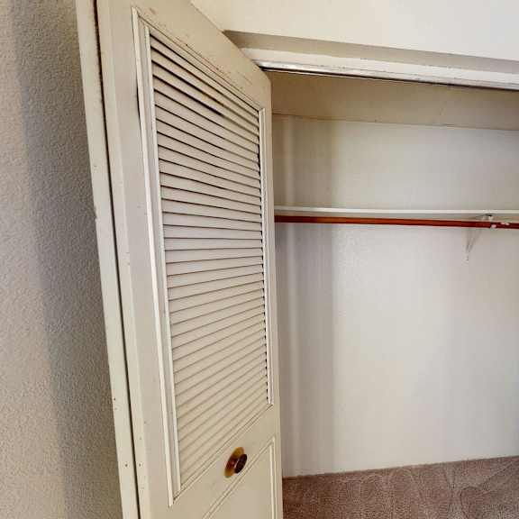 empty closet here at college view apartments with open louvered doors, revealing a wooden clothes rod and beige carpet. the ambiance is simple and neutral.