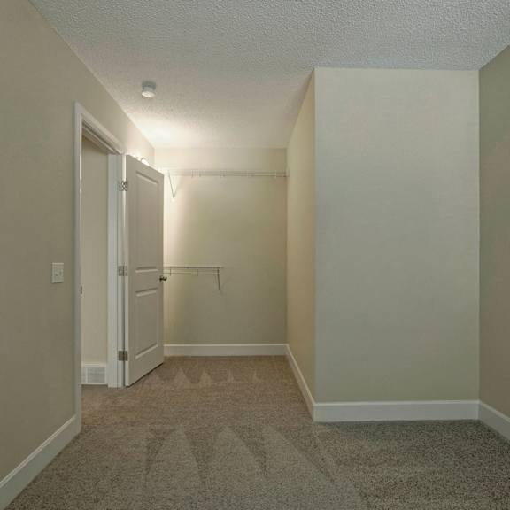 empty bedroom here at 3600 brentwood apartment homes with beige walls, an open white door, and a small closet with a wire shelf. the carpet is gray, creating a calm, neutral tone.