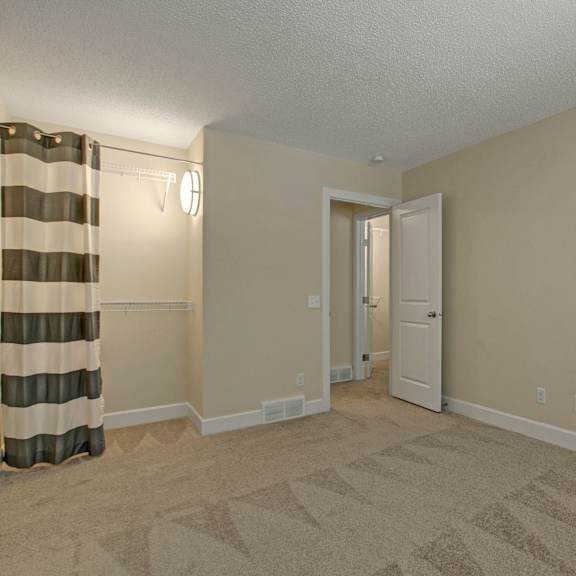 empty beige bedroom here at 3600 brentwood apartment homes with carpeted floor, open door, and striped curtains. wall sconces illuminate shelves on each side, creating a neutral, calm ambiance.