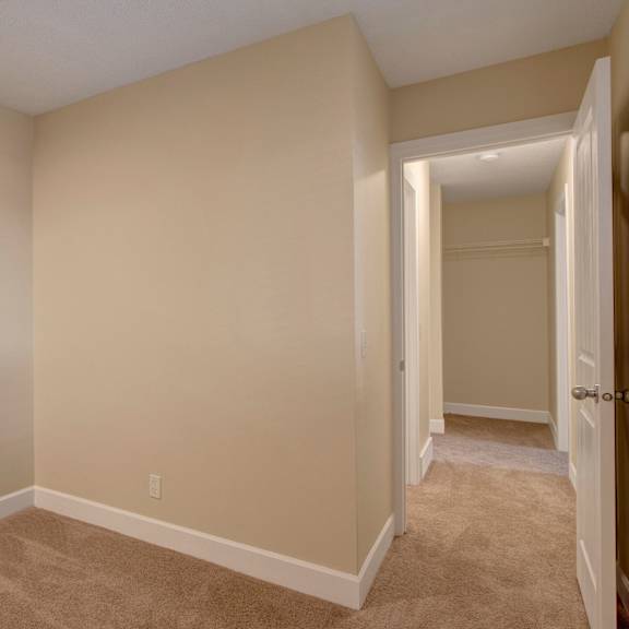 empty beige bedroom here at 3600 brentwood apartment homes with beige carpet and open closet. a small hallway leads to another similar room. calm, neutral atmosphere.