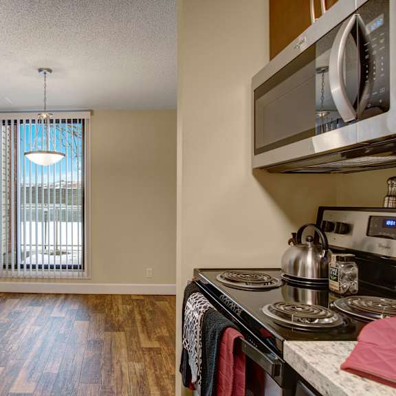 a modern kitchen here at 3600 brentwood apartment homes features stainless steel appliances, hardwood floors, and a bright window with vertical blinds. the atmosphere is warm and inviting.