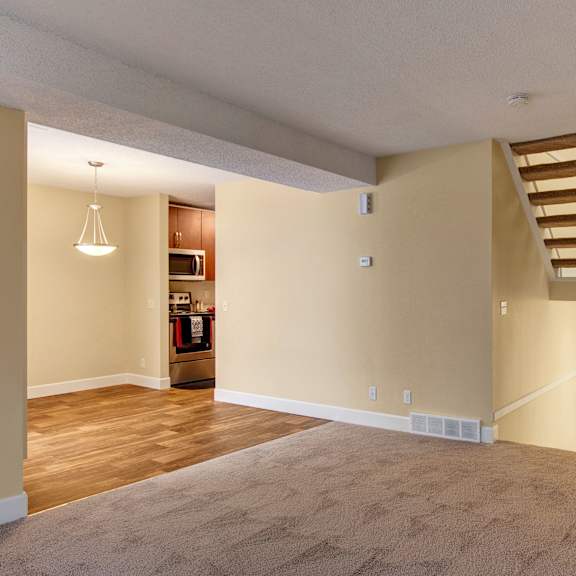 open living space here at 3600 brentwood apartment homes with beige walls and carpet, featuring a staircase with natural wood steps. adjacent kitchen with wood floors and stainless steel appliances.