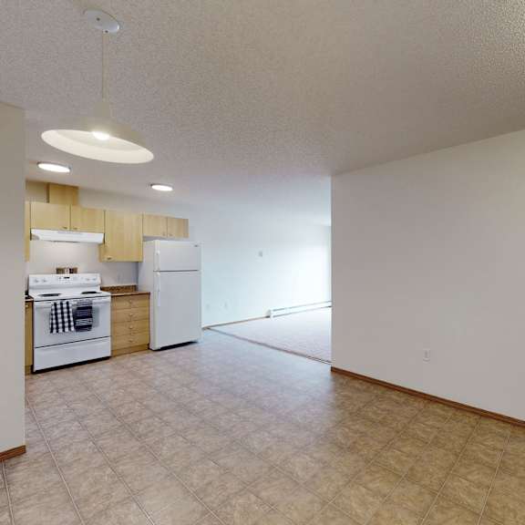 spacious kitchen and open living area here at birch terrace apartment homes with light wood cabinets, white appliances, tiled floor, and natural light. neutral tones evoke a welcoming feel.