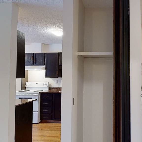narrow hallway view showing a kitchen here at broadmoor apartment homes with dark cabinets and white appliances to the left. on the right, a laundry area with a washer, dryer, and vent pipe.