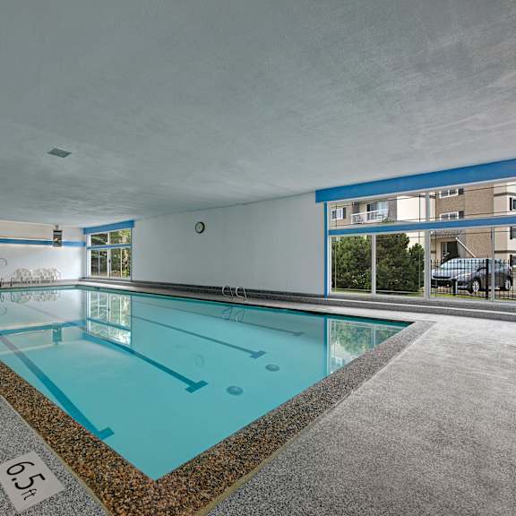 an indoor swimming pool here at cambridge west apartment homes with clear blue water, surrounded by a gray tile floor. large windows on the right let in natural light, reflecting off the pool.