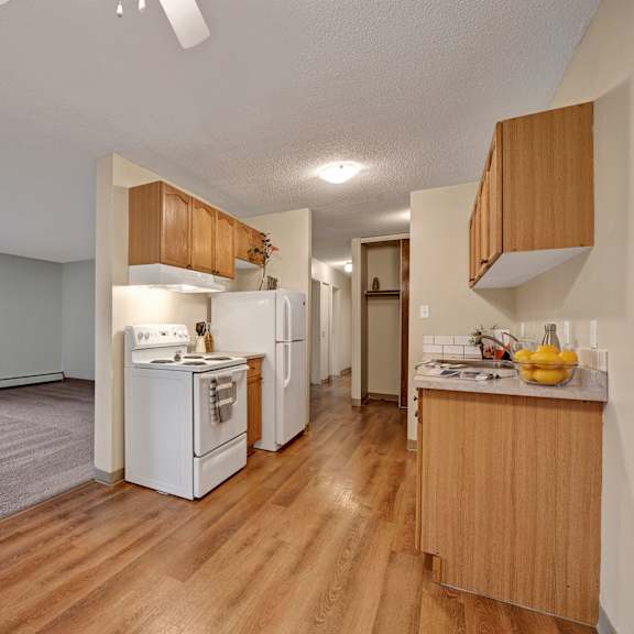 spacious apartment interior here at cambridge west apartment homes with open-plan kitchen and living area. kitchen features wooden cabinets, white appliances, and a fruit bowl on the counter.