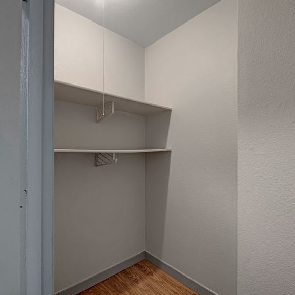 small empty closet here at cedar gardens apartment homes with two simple white shelves on beige walls. the space is lit by a ceiling light, casting a neutral, minimalistic tone.