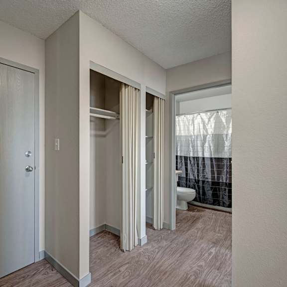 compact hallway here at cedar gardens apartment homes with a light gray entry door on the left, adjacent closet with sliding doors, and a glimpse into a bathroom with a white and black shower curtain.
