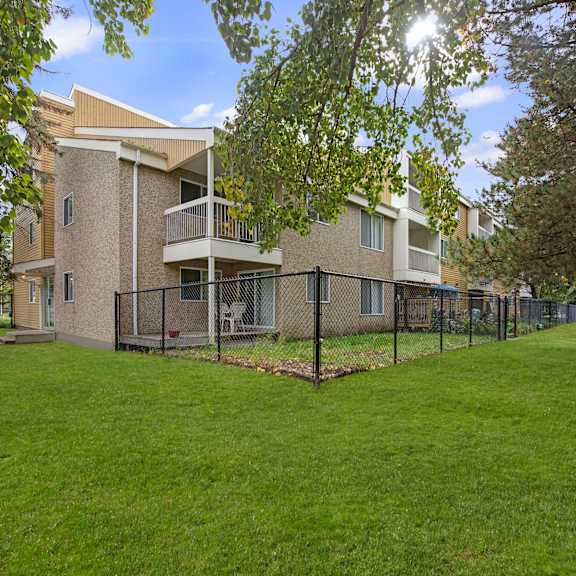 gateway gardens apartment homes complex with beige exterior and balconies, surrounded by a black fence and lush green lawn. large trees provide shade, creating a serene atmosphere.