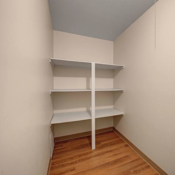 compact storage area here at gateway gardens apartment homes with three white shelves on cream walls. wooden floor adds warmth. neat and functional, with a calm, minimalistic feel.