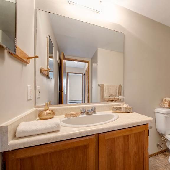 simple bathroom here at gateway square apartment homes with wooden vanity, oval mirror, and beige countertop. white toilet and bathtub. soft lighting creates a clean, inviting atmosphere.