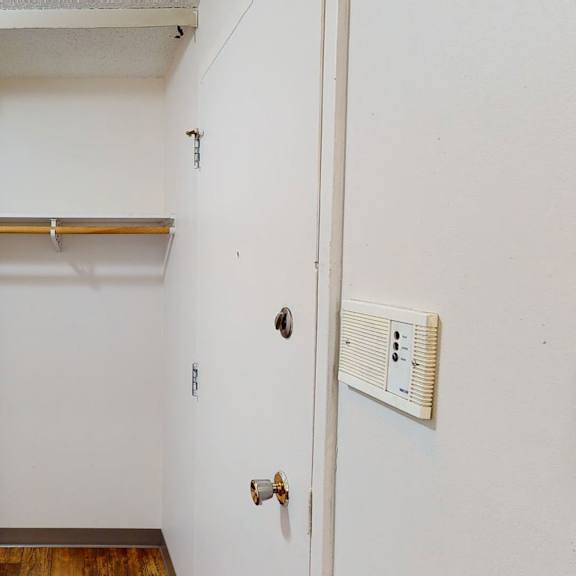 empty white closet here at lakewood heights apartment homes with a wooden rod and shelf, adjacent to a door with a round knob. a light switch and intercom are mounted on the wall.