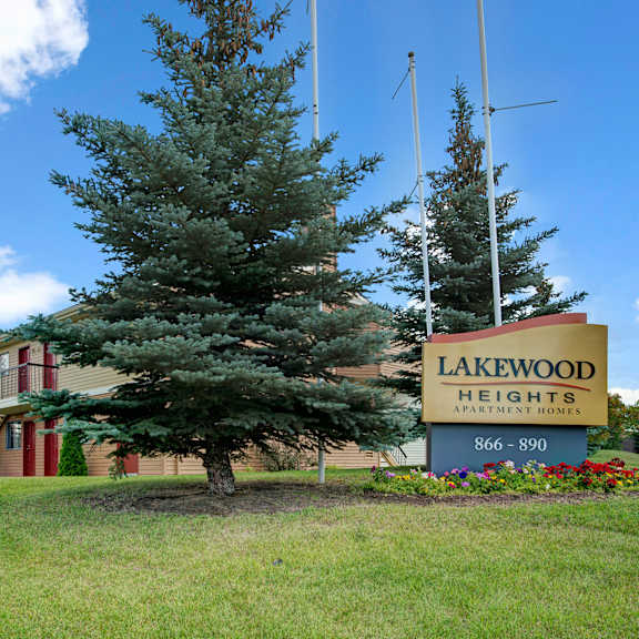 sign for lakewood heights apartment homes set on a manicured lawn with colorful flowers and tall evergreen trees. a clear, sunny sky above.