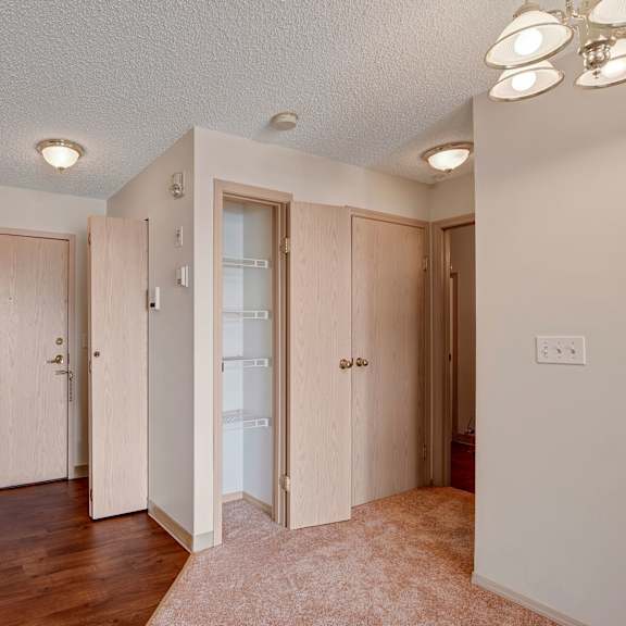 simple room interior here at manning crossing apartment homes with beige walls, wooden doors, white closets, and mixed flooring. three lights illuminate the space, creating a cozy atmosphere.