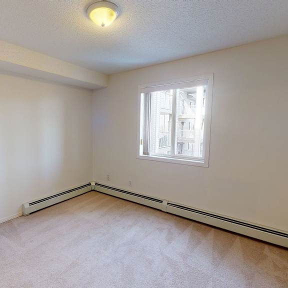 a small, empty room here at somerset pointe apartment homes with white walls and beige carpet. a window lets in natural light, showing a view of neighboring buildings. it's simple and neutral.