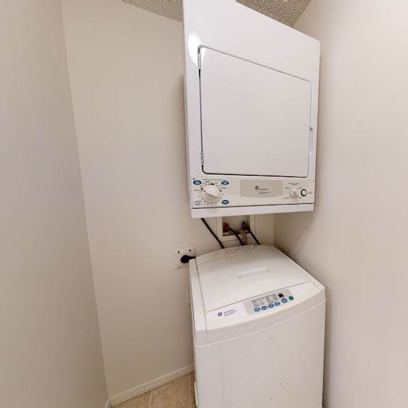 compact laundry room here at somerset pointe apartment homes with a beige wall features a stacked white washer and dryer. the setting is minimalistic, conveying cleanliness and simplicity.