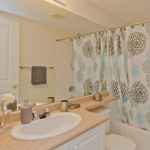 bathroom here at somerset pointe apartment homes with beige walls, featuring a sink, soap dispenser, and decorative items on the countertop. blue and brown floral shower curtain adds a touch of color.