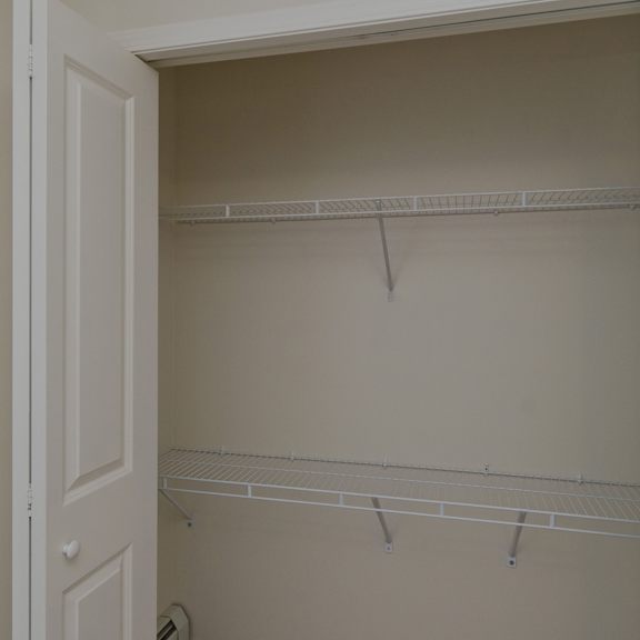 open closet here at somerset pointe apartment homes with white double doors, featuring two wire shelves against beige walls. the space is empty, conveying a clean, minimalistic tone.