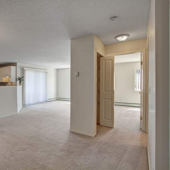 bright, empty apartment interior here at somerset pointe apartment homes featuring a spacious living area with beige carpet, white walls, and a cozy kitchen with white cabinetry and appliances.