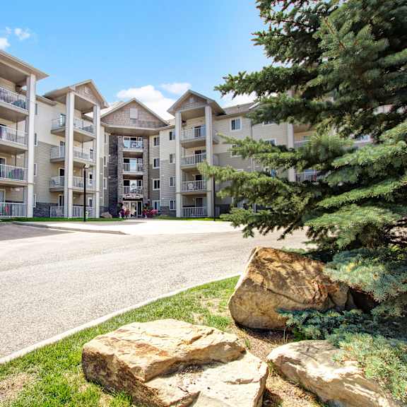 four-story somerset pointe apartment homes complex with beige siding and stone accents, surrounded by greenery and pine trees under a clear blue sky. relaxed atmosphere.