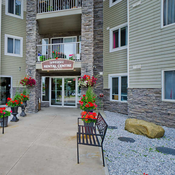 entrance of somerset rental centre features stone accents, elegant benches, vibrant red and white flowers for a welcoming, inviting atmosphere.