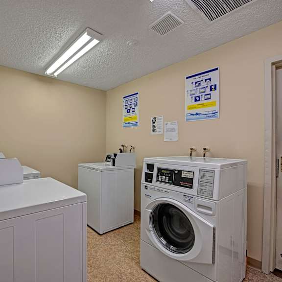 laundry room here at sterling place apartment homes with two top-loading washers and a front-loading dryer. beige walls, fluorescent lighting, and instructional posters hang on the walls. clean and functional atmosphere.