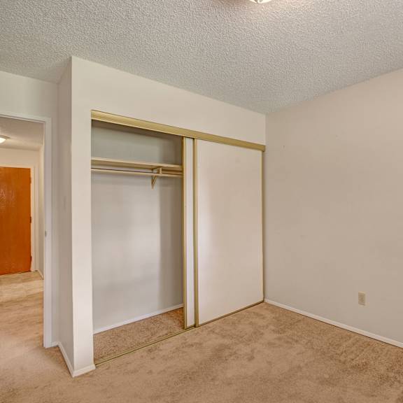 empty room here at sterling place apartment homes with beige carpet and light beige walls. a small closet with sliding doors is on the left, next to an open door leading to a hallway.