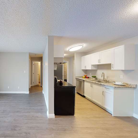 spacious apartment interior here at wyndham crossing apartment homes with light gray walls and wood flooring. open living area with large window on the left; modern kitchen on the right.