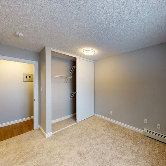 empty beige carpeted room here at wyndham crossing apartment homes with gray walls, a white closet with sliding doors on the left, ceiling light, open door, and a small window on the right.