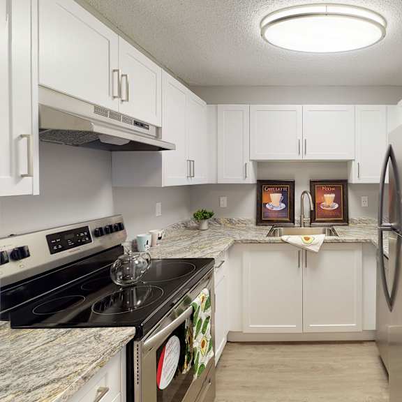 modern kitchen here at wyndham crossing apartment homes with white cabinets and granite countertops. stainless steel appliances, including a fridge and stove. bright, inviting atmosphere.