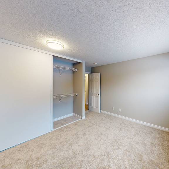 empty room here at wyndham crossing apartment homes with beige carpet, light gray walls, and an open white closet. a door on the left leads to a lit hallway. the atmosphere is clean and minimal.
