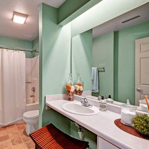 a bright bathroom here at river’s cove featuring a wide vanity, large mirror, white shower curtain, and green walls, creating a fresh, clean, and inviting space.