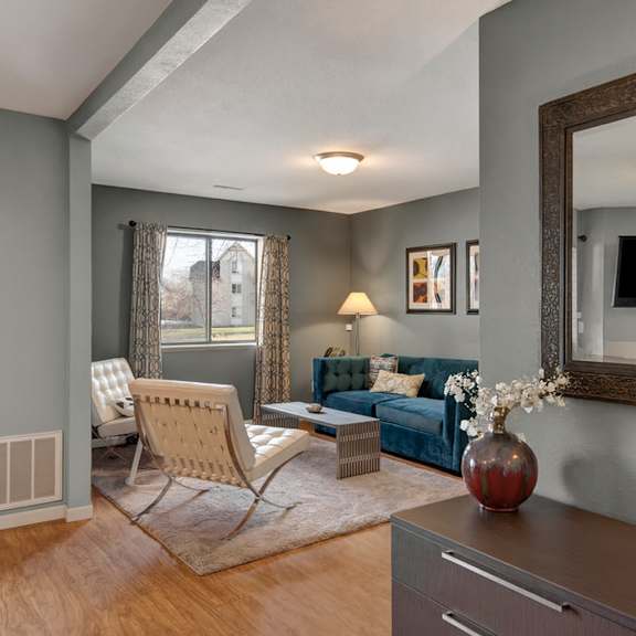a welcoming living room here at river’s cove with a blue sofa, cream accent chairs, and warm wood flooring. large windows and soft lighting create a bright, comfortable space perfect for relaxing.