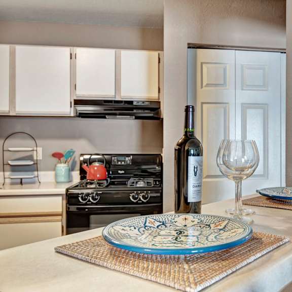 a bright kitchen here at river’s cove featuring a breakfast bar with decorative blue plates, wine glass, and bottle. light cabinetry and an open pass-through create a clean, inviting space perfect for casual dining.