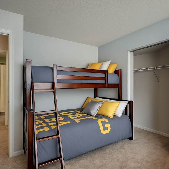 a cozy bedroom here at river’s cove featuring a wooden bunk bed with gray and yellow bedding, soft carpet, and an open closet, creating a warm, functional, and inviting space.